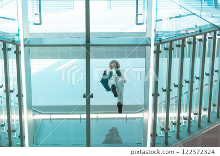 A view from below through a transparent glass floor of a woman in a modern business center. Modern architecture A view from below through a transparent glass floor of a woman in a modern business center. Modern architecture 122572324