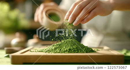 Green tea powder being sprinkled onto wooden surface, creating vibrant mound 122573067