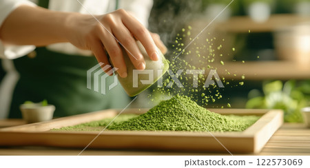 hand sprinkles green tea powder onto wooden tray, creating vibrant scene 122573069