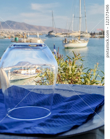Fishing boat visible through a drinking glass inverted over a plate with other boats visible in the background in a harbour Fishing boat visible through a drinking glass inverted over a plate with other boats visible in the background in a harbour 122573406