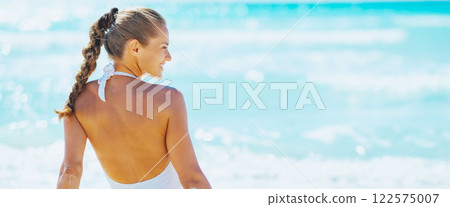 Young woman sitting at seaside and looking on copy space. rear v 122575007