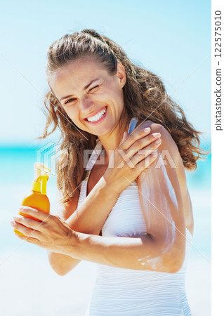 Smiling young woman applying sun block creme on beach 122575010