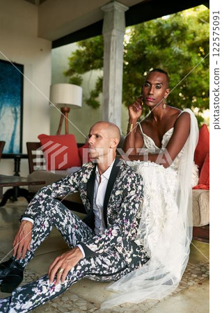 Ambiguous gender fluid person in white bridal dress with LGBTQ partner in bold floral suit at exotic villa wedding. Couple embraces inclusive love. Stylish, vibrant, modern ceremony. 122575091