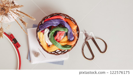 Basket with colored floss and canvas for embroidery on a gray top view web banner 122576175
