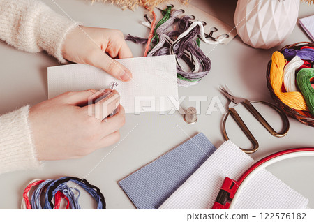 Female hands cross stitching on canvas on table among equipment 122576182
