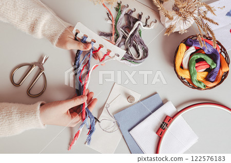 Female hands holding a set of colored embroidery floss on a work table top view Female hands holding a set of colored embroidery floss on a work table top view 122576183