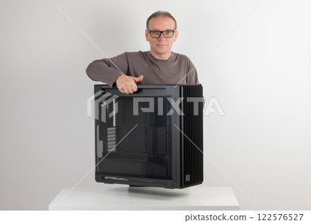 Man holding a heavy PC case, weight 15,8 kg, empty big tower, chassis, on side is tempered-glass. Man holding a heavy PC case, weight 15,8 kg, empty big tower, chassis, on side is tempered-glass. 122576527