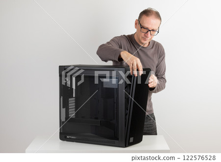 Man removing  15.5 mm front panel grille with 45% porosity with dust filter from  PC case, empty big tower, chassis, on side is tempered-glass. 122576528