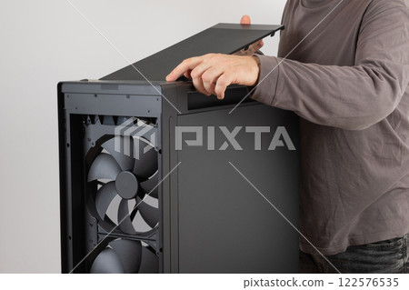 Man installing  top panel with dust filter from  PC case, empty big tower, chassis. Under top panel is place for 420 mm radiator for AIO cooling 122576535
