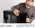 Man removing  15.5 mm front panel grille with 45% porosity with dust filter from  PC case, empty big tower, chassis, on side is tempered-glass. 122576573