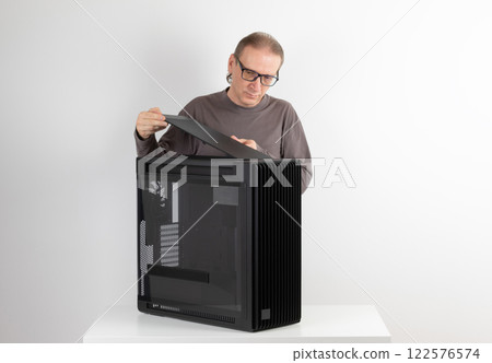 Man installing  top panel with dust filter to  PC case, empty big tower, chassis. Under top panel is place for 420 mm radiator for AIO cooling 122576574
