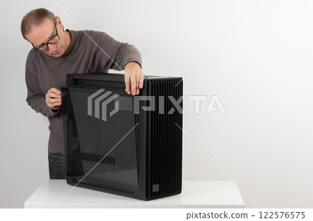 Man removing  tempered-glass left panel from  PC case, empty big tower, chassis. 122576575