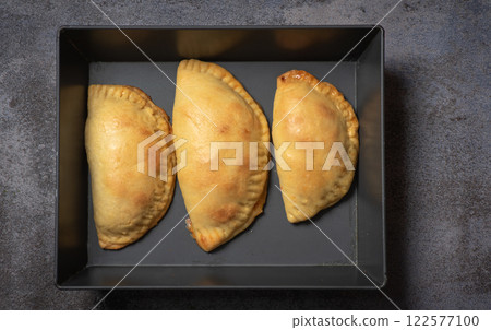 Golden-baked empanadas on a black tray 122577100