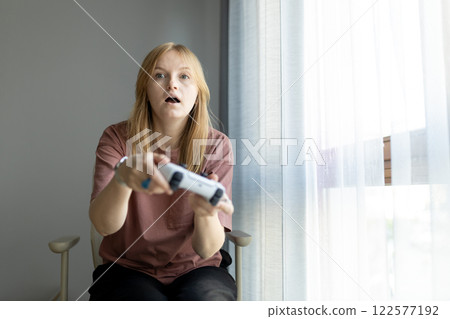 Happy blonde girl playing video game at home. Woman in casual clothes holding wireless controller playing video game. Entertainment, technology and hobby concept Happy blonde girl playing video game at home. Woman in casual clothes holding wireless controller playing video game. Entertainment, technology and hobby concept 122577192