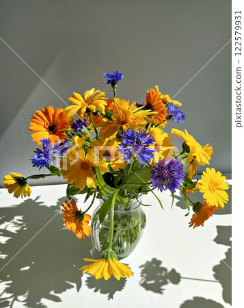 Cheerful bouquet of calendula and cornflowers in glass vase. Simple bouquet is rustic style. Summer flowers bouquet concept 122579931