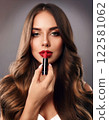 A woman with long hair applying red lipstick (front view) 122581062
