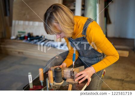Pedant woman joiner works in joinery workshop, sanding, turning wooden knife blanks on lathe Pedant woman joiner works in joinery workshop, sanding, turning wooden knife blanks on lathe 122581719