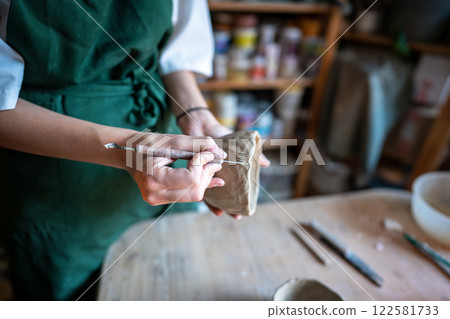 Potter hand carving pattern on clay bowl with knife in workshop. Manual labor, creative ceramic work Potter hand carving pattern on clay bowl with knife in workshop. Manual labor, creative ceramic work 122581733