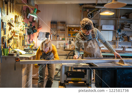 Carpentry colleagues handle circular saw station, measure wood beam with precision. Family business 122581736