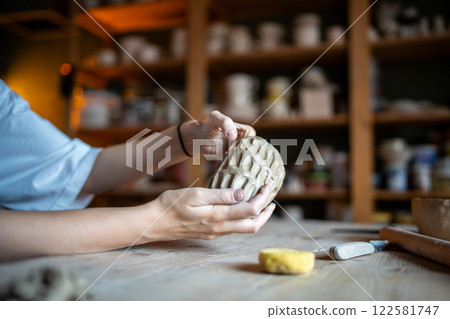 Molding craft ceramics: table in pottery studio with female artist shaping wet clay for potter bow Molding craft ceramics: table in pottery studio with female artist shaping wet clay for potter bow 122581747