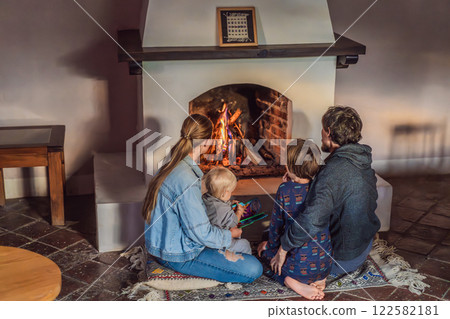 Family bonding by the fireplace during cozy winter evening. Warm and peaceful family moment indoors. Togetherness, love, and relaxation concept. A warm and inviting scene featuring a lit fireplace Family bonding by the fireplace during cozy winter evening. Warm and peaceful family moment indoors. Togetherness, love, and relaxation concept. A warm and inviting scene featuring a lit fireplace 122582181