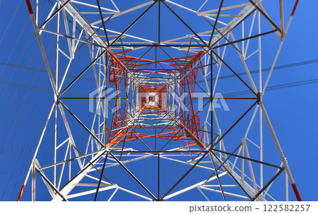 A geometric pattern of high voltage towers towering into the blue sky seen from below 122582257