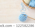 Light blue knitting, yarn and basket on a wooden desk 122582286