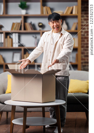 opening delivery box, excited man, Online shopping concept, middle-aged man joyfully opens a large cardboard box in a stylish living room. He expresses delight, revealing the surprise inside while opening delivery box, excited man, Online shopping concept, middle-aged man joyfully opens a large cardboard box in a stylish living room. He expresses delight, revealing the surprise inside while 122582553