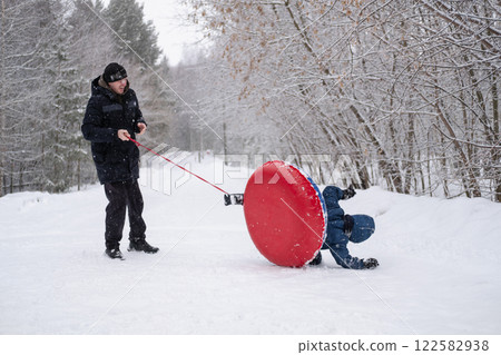 a child flips over from snow tubing while riding with his dad against the backdrop of a winter forest. Dangerous skiing in winter. Children's injuries during winter sports 122582938