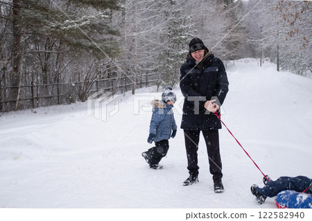 dad in winter jacket rides child on snow tubing around himself, against the background of snowfall and forest in winter. Dangerous and fun games of dad and son in winter dad in winter jacket rides child on snow tubing around himself, against the background of snowfall and forest in winter. Dangerous and fun games of dad and son in winter 122582940