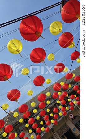 Vibrant red and yellow lanterns suspended across open balconies under a serene blue sky, representing festive celebrations of chinese new year and traditional cultural decor 122583059