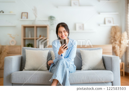 Smiling pretty young Asian woman sitting on cozy couch 122583503