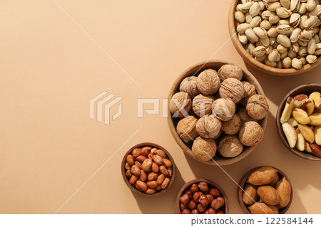 Various nuts in wooden bowls on a beige background Various nuts in wooden bowls on a beige background 122584144