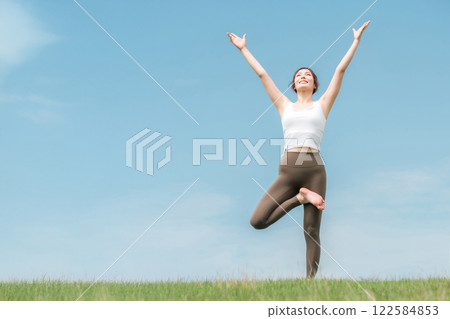 A woman doing yoga and pilates in a park with a blue sky (tree pose) 122584853