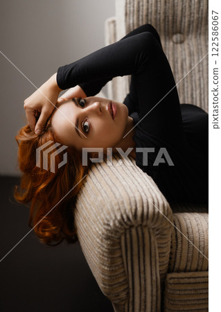 Elegant redhead woman with long hair leaning back in chair looking at camera 122586067