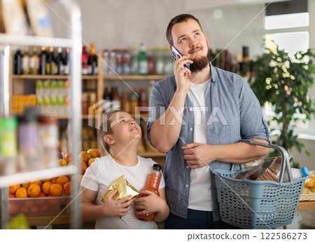 Young man talking on phone while grocery shopping with teenage son 122586273
