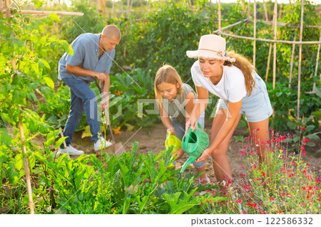 Daughter helps mom to water plants from watering can in farm field Daughter helps mom to water plants from watering can in farm field 122586332