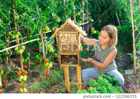 Portrait of happy girl next to hotel for insects in of wooden birdhouse in garden 122586355