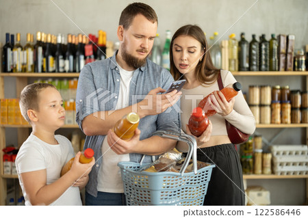 Family choose bottles of juice and scan QR code with smartphone in shop Family choose bottles of juice and scan QR code with smartphone in shop 122586446