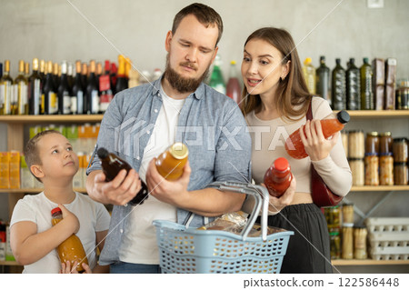 Preteen boy with mom and dad choosing juices in supermarket Preteen boy with mom and dad choosing juices in supermarket 122586448
