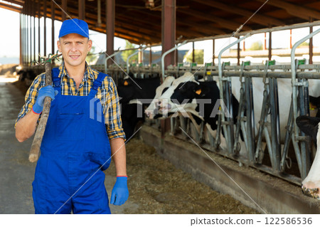 Farmer with pitchfork in hands in cowhouse 122586536