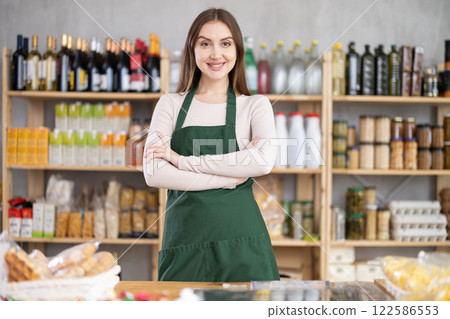 Portrait of positive female seller in an apron behind the counter of grocery store 122586553