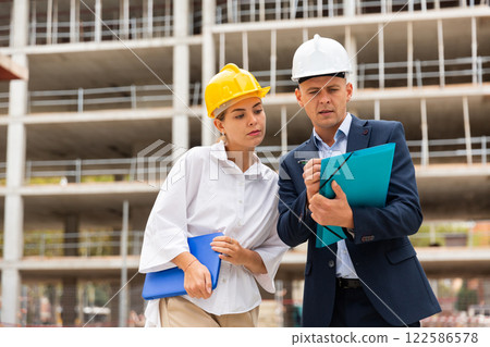 Two young successful architects on the construction site, discuss the construction plan 122586578