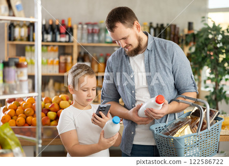 European man with son customer at shop scans QR code on milk bottle using phone camera 122586722