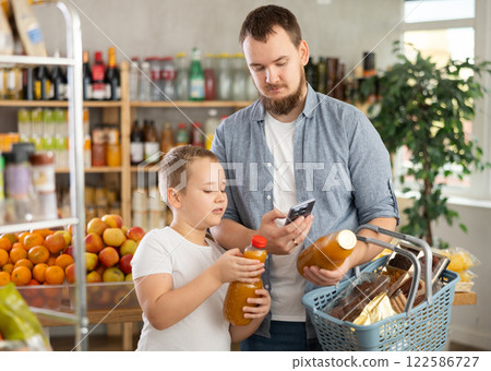 European man with son customer at shop scans QR code on juice bottle using phone camera European man with son customer at shop scans QR code on juice bottle using phone camera 122586727