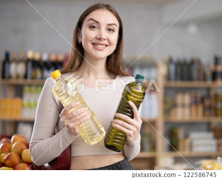 Girl buyer looks thoughtfully and indecisively at bottles of vegetable oil Girl buyer looks thoughtfully and indecisively at bottles of vegetable oil 122586745