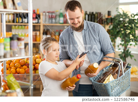 European man with son customer at shop scans QR code on juice bottle using phone camera 122586746
