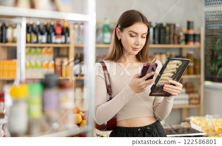 European young woman customer at shop scans QR code on Jiaozi package using phone camera European young woman customer at shop scans QR code on Jiaozi package using phone camera 122586801