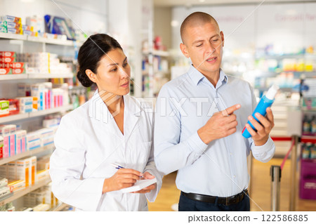 Female specialist is helping male client choose medicine in pharmacy closeup Female specialist is helping male client choose medicine in pharmacy closeup 122586885