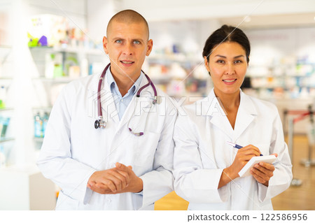 Portrait of two pharmacists - men and women in white coats in pharmacy Portrait of two pharmacists - men and women in white coats in pharmacy 122586956